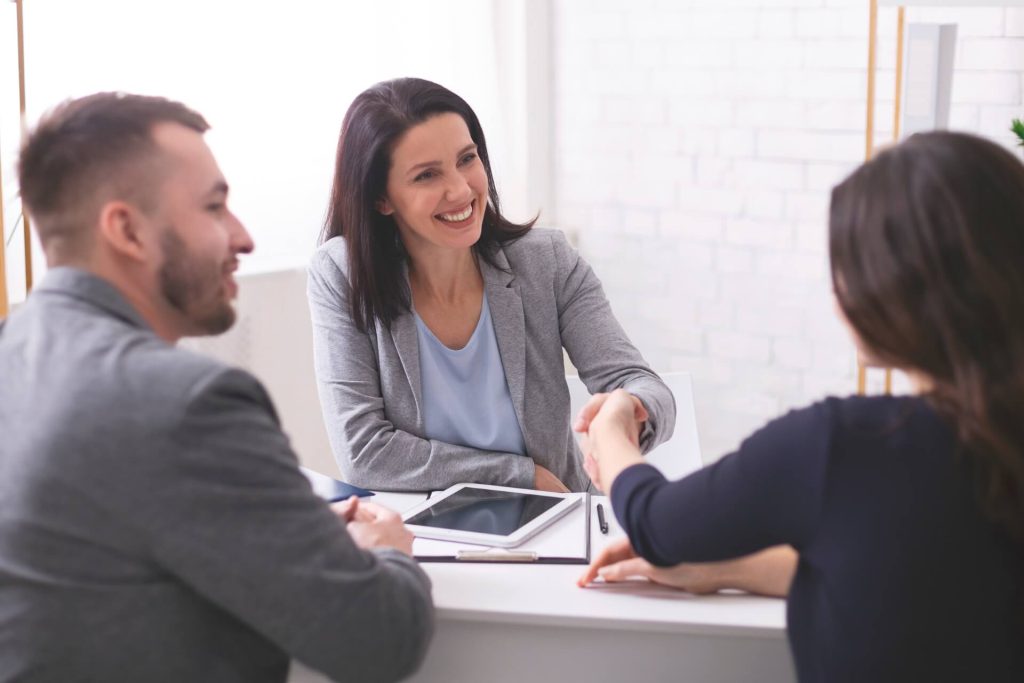 tres personas en una reunión y dos mujeres estrechando la mano